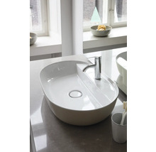 Ovales Aufsatzwaschbecken aus weißer Keramik mit verchromter Armatur in einem hellen, modernen Badezimmer auf einer Steinplatte.