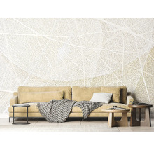 Papier peint panoramique avec motif de structure de feuille dans un salon lumineux derrière un canapé avec coussins et tables basses.