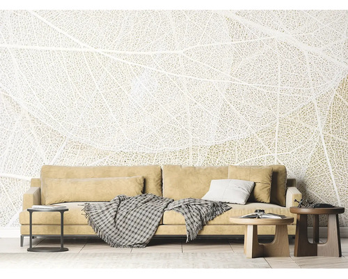 Papier peint panoramique avec motif de structure de feuille dans un salon lumineux derrière un canapé avec coussins et tables basses.