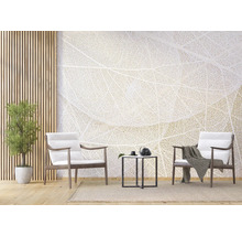 Salon lumineux avec papier peint panoramique motif nervures de feuilles, deux fauteuils en bois avec coussins blancs, table d'appoint noire et plante.