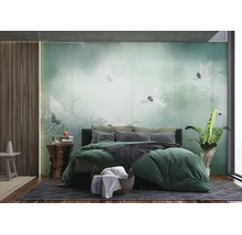 Papier peint photo en chambre avec grues blanches en forêt brumeuse, lit vert avec coussins, panneaux en bois au mur et plante verte.