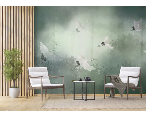Papier peint panoramique avec des grues blanches au-dessus d'une forêt de brume verte dans un salon moderne avec fauteuils en bois.