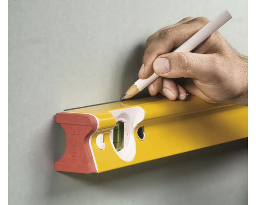 Une main trace une ligne avec un crayon le long d'un niveau à bulle Stabila sur un mur.