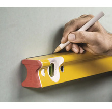 Une main trace une ligne avec un crayon le long d'un niveau à bulle Stabila sur un mur.