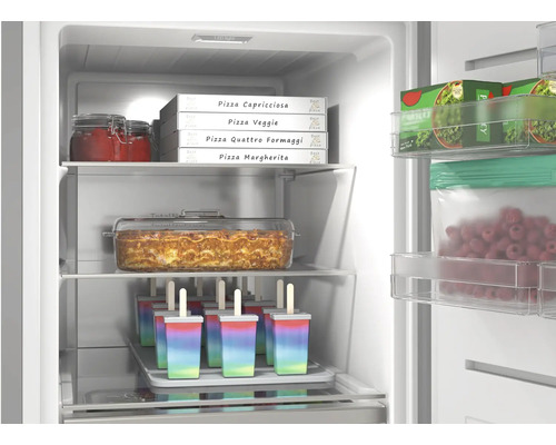 Intérieur d'un congélateur avec divers aliments surgelés tels que pizzas, lasagnes, glaces à l'eau et baies sur des tablettes en verre.
