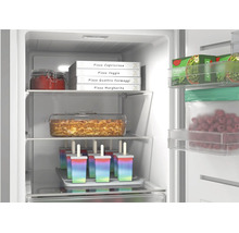 Congélateur bien organisé avec boîtes de pizza, plat à lasagne et bâtonnets glacés. Éclairage intérieur lumineux et clayettes en verre.