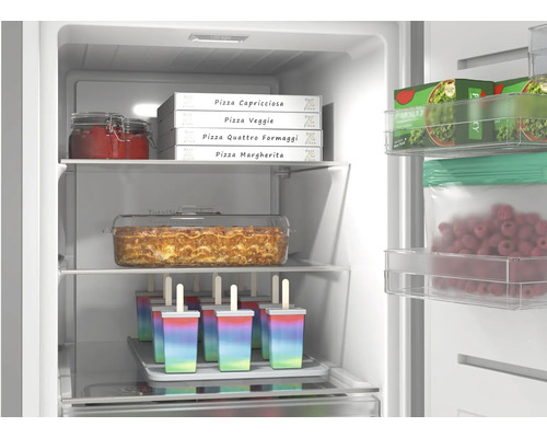 Congélateur bien organisé avec boîtes de pizza, plat à lasagne et bâtonnets glacés. Éclairage intérieur lumineux et clayettes en verre.