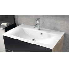 Lavabo blanc moderne avec mitigeur chromé sur un meuble sous-vasque sombre devant un mur gris.