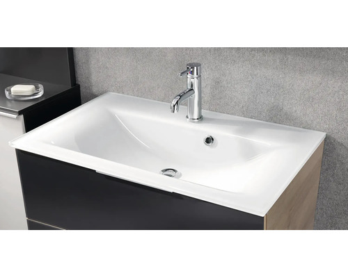 Lavabo blanc moderne avec mitigeur chromé sur un meuble sous-vasque sombre devant un mur gris.