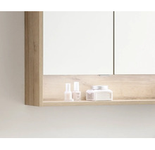 Badezimmer-Spiegelschrank mit offenem Ablagefach in Holzoptik, auf dem Pflegeprodukte stehen.