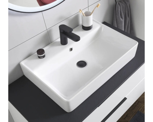 Vasque à poser rectangulaire en céramique blanche avec un robinet noir sur un plan de toilette sombre dans une salle de bains.