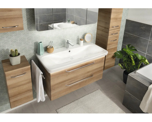 Modernes Badezimmermöbel-Set in Eiche-Optik mit weißem Waschtisch, passenden Schränken, großem Spiegel und gemusterter Tapete.