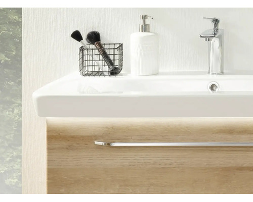 Moderner Waschplatz mit weißem Waschbecken, verchromter Armatur, Seifenspender und Waschtischunterschrank in Holzoptik mit LED Beleuchtung.