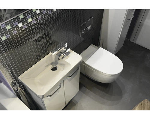 Salle de bain moderne avec meuble sous-lavabo blanc, lavabo en céramique, WC suspendu et mur en mosaïque sombre.