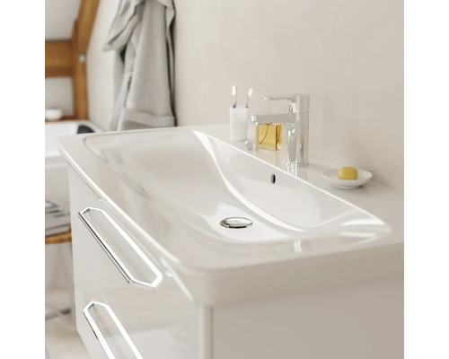 Meuble sous-vasque blanc moderne avec deux tiroirs, poignées argentées et lavabo en céramique intégré dans une salle de bains lumineuse.