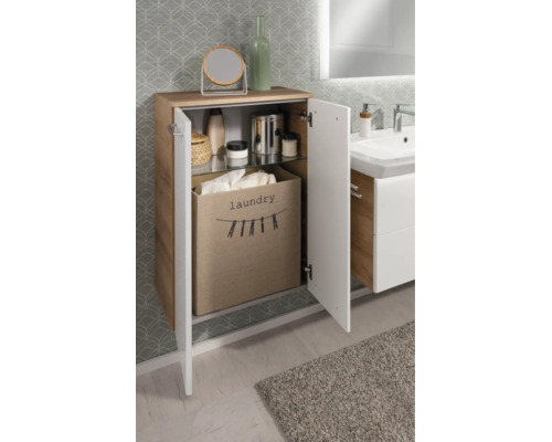 Armoire de salle de bain aspect bois, façades blanches, porte ouverte, panier à linge en tissu et étagère en verre.