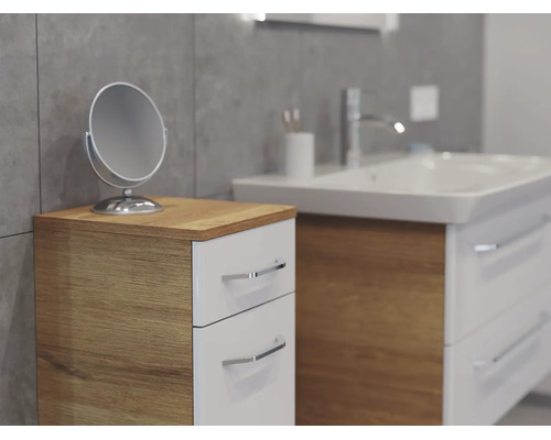 Moderner Badezimmer-Beistellschrank mit zwei weißen Schubladen und Korpus in Holzoptik neben einem Waschtisch mit Kosmetikspiegel.