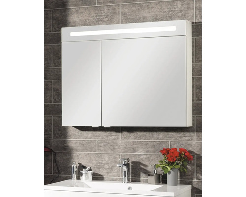 Spiegelschrank mit LED-Beleuchtung und zwei Spiegeltüren über einem Waschbecken an einer grauen Fliesenwand.