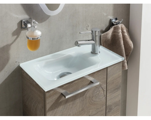 Lavabo moderne avec vasque en verre blanc, meuble sous-vasque aspect bois, mitigeur chromé, distributeur de savon et crochet porte-serviette.