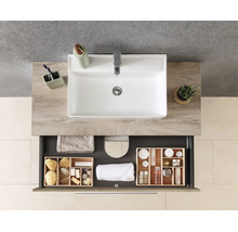 Meuble de salle de bain avec lavabo blanc sur plan de travail aspect bois et tiroir ouvert avec organisateurs pour accessoires.