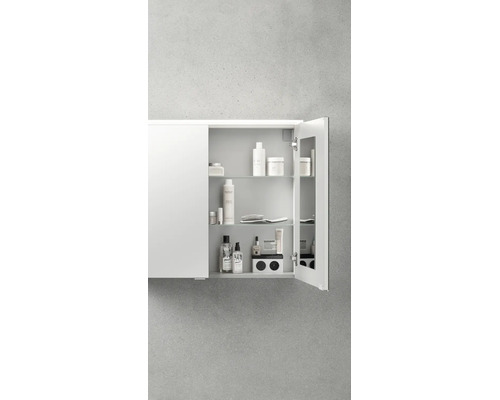 Armoire de toilette blanche ouverte avec trois étagères en verre et une prise de courant intégrée, organisée avec divers articles de toilette.
