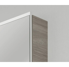 Gros plan de l'angle d'une armoire de toilette avec cadre blanc et paroi latérale aspect bois.