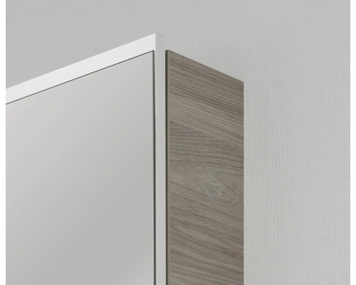 Gros plan de l'angle d'une armoire de toilette avec cadre blanc et paroi latérale aspect bois.