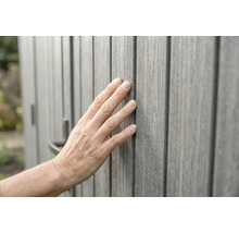 Hand berührt graue Wandverkleidung in Holzoptik mit fühlbarer Oberflächenstruktur.