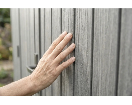 Hand berührt graue Wandverkleidung in Holzoptik mit fühlbarer Oberflächenstruktur.