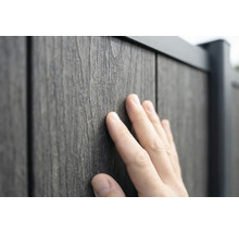 Une main touche la surface texturée d'un panneau de clôture aspect bois en composite bois-plastique.