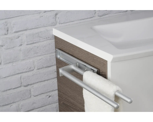 Porte-serviettes télescopique à deux barres en métal, monté sur un meuble de salle de bains aspect bois à côté d'un lavabo blanc.