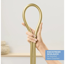 Une main tient un flexible de douche doré pour démontrer sa conception anti-torsion.