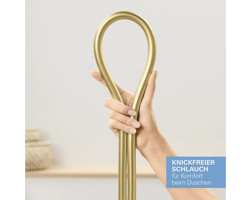 Une main tient un flexible de douche doré pour démontrer sa conception anti-torsion.
