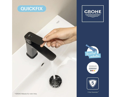 Main actionnant un mitigeur Grohe noir sur lavabo blanc. Symboles: QuickFix, outil, design allemand, cinq ans de garantie. Grohe Logo.