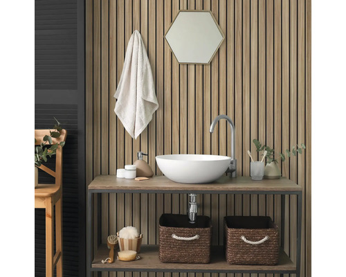 Panneau acoustique avec lamelles en bois sur un mur de salle de bain derrière un lavabo avec vasque blanche et miroir hexagonal.