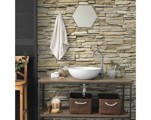Salle de bains moderne avec parement mural en pierre structurée, lavabo à poser sur une étagère en bois et miroir hexagonal.