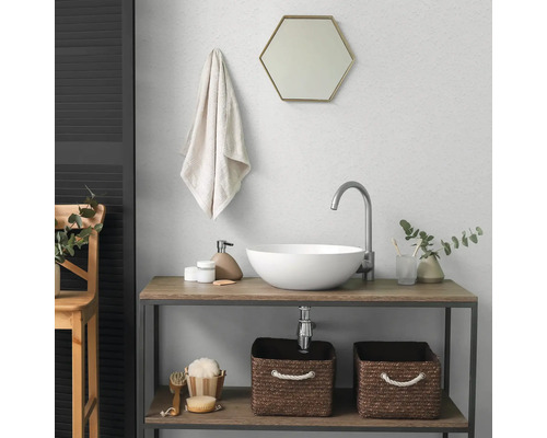 Salle de bains moderne avec vasque à poser blanche, robinet haut, miroir hexagonal et meuble sous vasque en bois avec paniers de rangement.