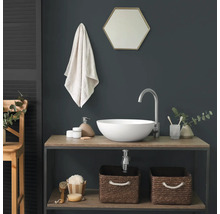 Salle de bains moderne avec une vasque à poser ronde blanche sur un meuble en bois, un robinet argenté haut et un miroir hexagonal sur un mur sombre.