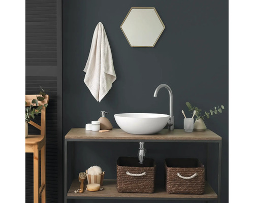 Salle de bains moderne avec une vasque à poser ronde blanche sur un meuble en bois, un robinet argenté haut et un miroir hexagonal sur un mur sombre.