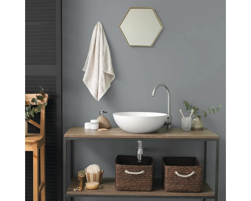 Salle de bain moderne avec vasque à poser blanche sur meuble sous-vasque en bois, robinet haut, miroir hexagonal et paniers tressés.