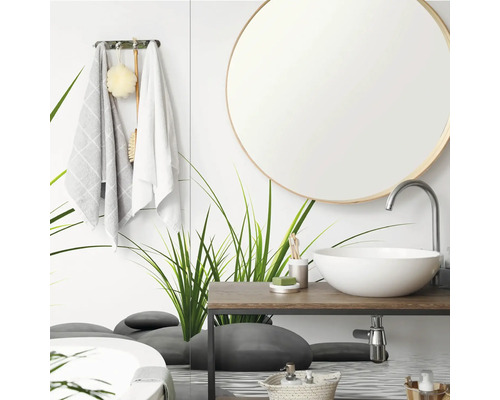 Salle de bains moderne avec miroir rond, vasque à poser blanche sur plan en bois et paroi en verre avec motifs d herbe et de galets.