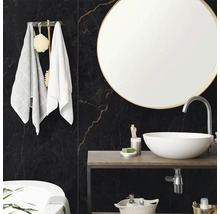 Salle de bain moderne avec carrelage mural aspect marbre noir, miroir rond et vasque blanche sur console en bois.