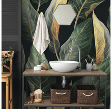 Papier peint photo avec de grandes feuilles botaniques dans une salle de bain derrière un meuble en bois avec vasque blanche et accessoires.
