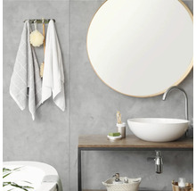 Salle de bains moderne avec miroir rond, vasque à poser blanche sur un plan de toilette en bois et mur gris aspect béton.