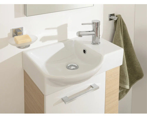 Salle de bains moderne avec lavabo compact, vasque en céramique blanche, meuble sous-vasque aspect bois, porte-savon et porte-serviette.