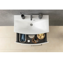 Vue de dessus d'un meuble de salle de bain blanc avec un tiroir ouvert contenant des articles de toilette, des serviettes et des éponges.