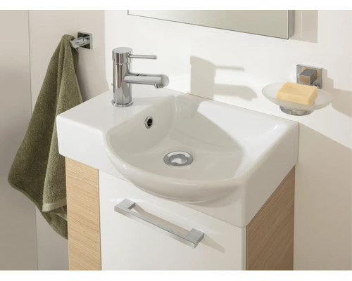 Petit lavabo moderne avec robinet chromé sur un meuble sous-vasque aspect bois avec crochet à serviette et porte-savon.