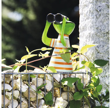 Figurine de jardin grenouille avec jumelles et haut rayé sur un gabion de pierres parmi des plantes grimpantes.