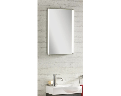 Miroir de salle de bain moderne avec éclairage LED vertical, lavabo blanc et robinet chromé sur un mur texturé.