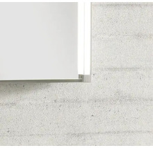 Gros plan sur le coin d'un miroir avec cadre métallique et éclairage latéral à LED intégré sur un mur texturé.